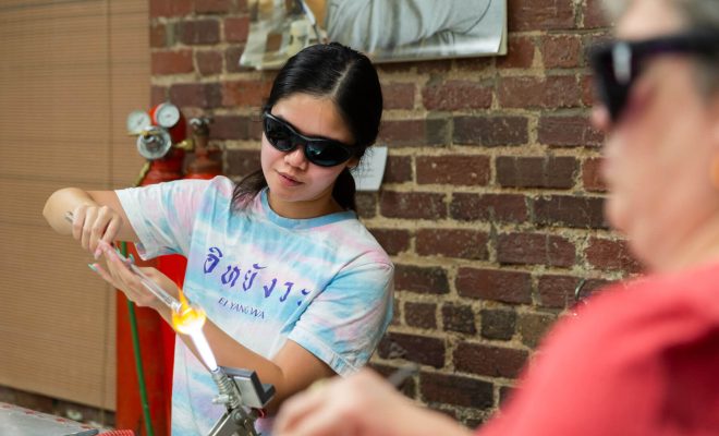 A young woman wearing safety glasses using a torch in a glassworking studio.