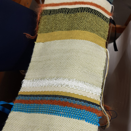 A colorful handwoven textile sample featuring striped patterns in green, yellow, white, and blue.