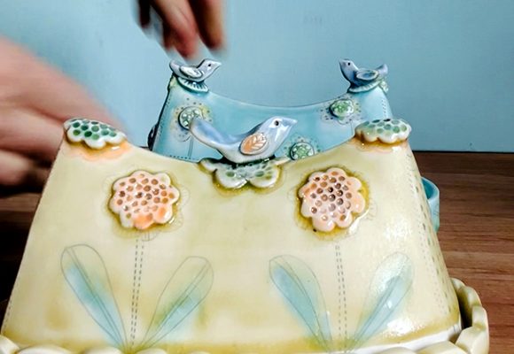 Hand placing a figurine on a decorated cake.