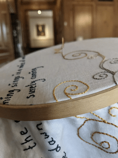 Image of fabric in a embroidery hoop with grey and tan stitching.