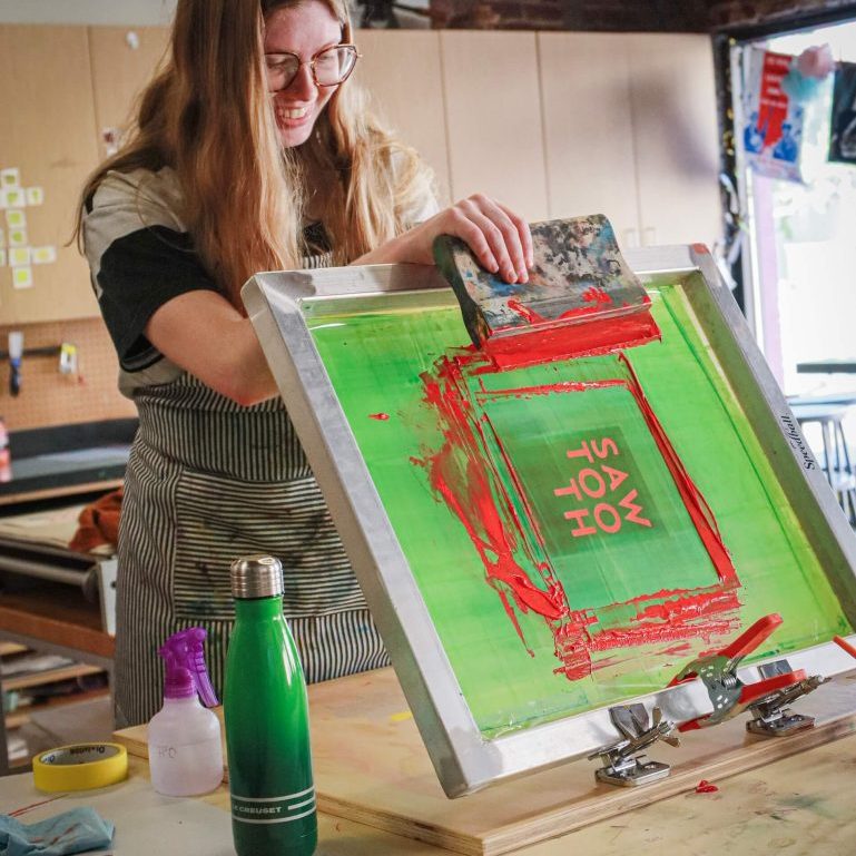 Woman using a squeegee to screen-print a green and red design.