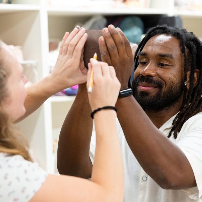 Two people collaborating on a clay sculpture in a studio.