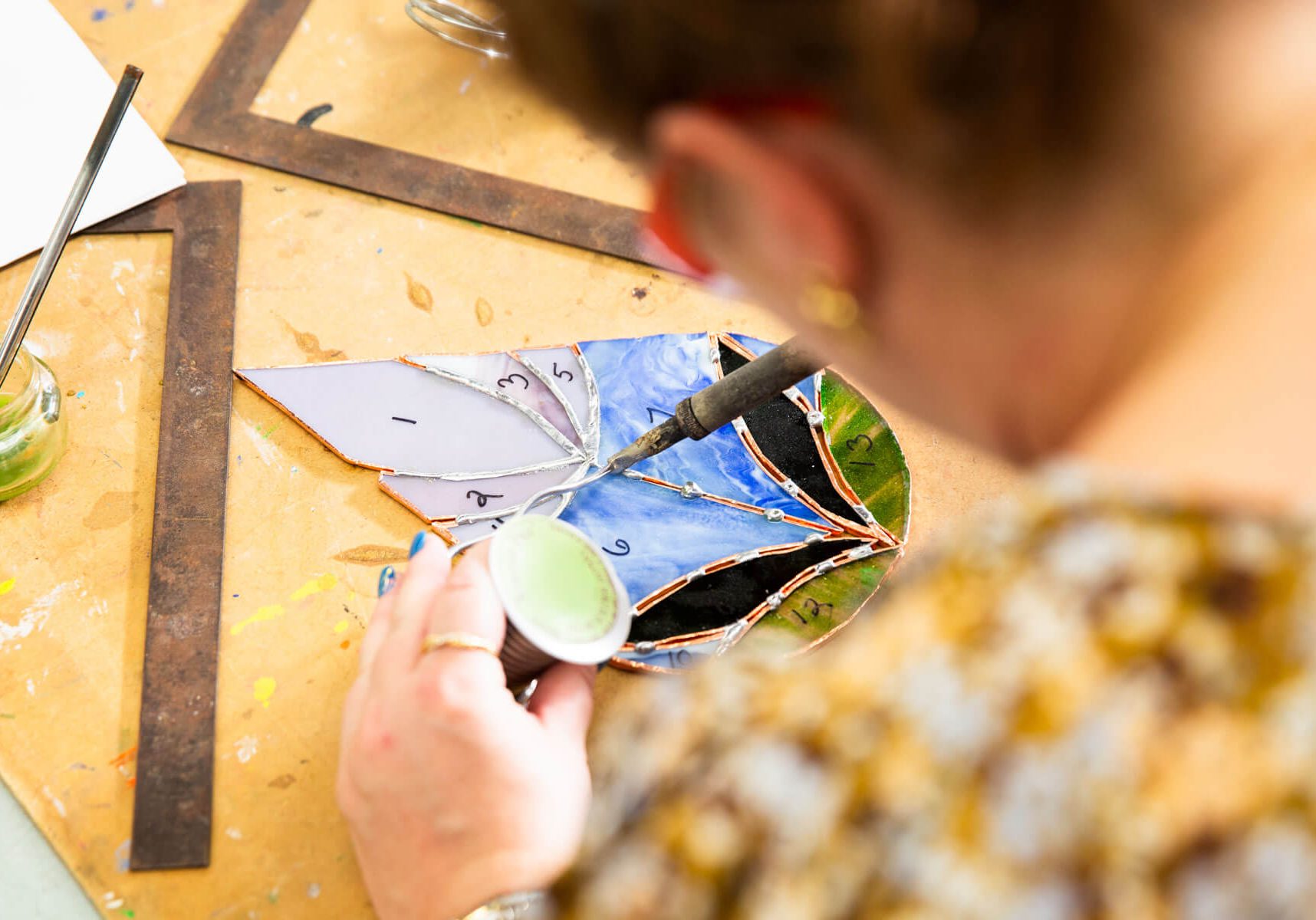 An artist soldering pieces of a stained glass project at a workbench.