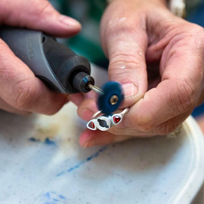 Close-up of hands polishing a silver ring using a rotary tool.