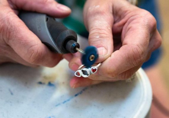 Close-up of hands polishing a silver ring using a rotary tool.