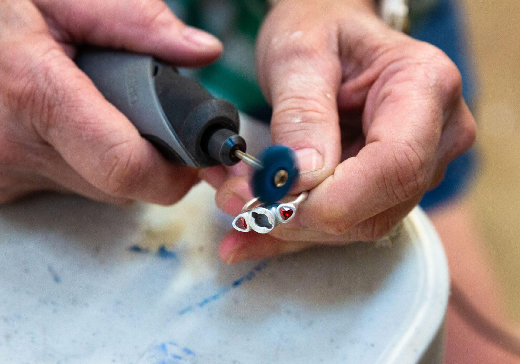 Close-up of hands polishing a silver ring using a rotary tool.