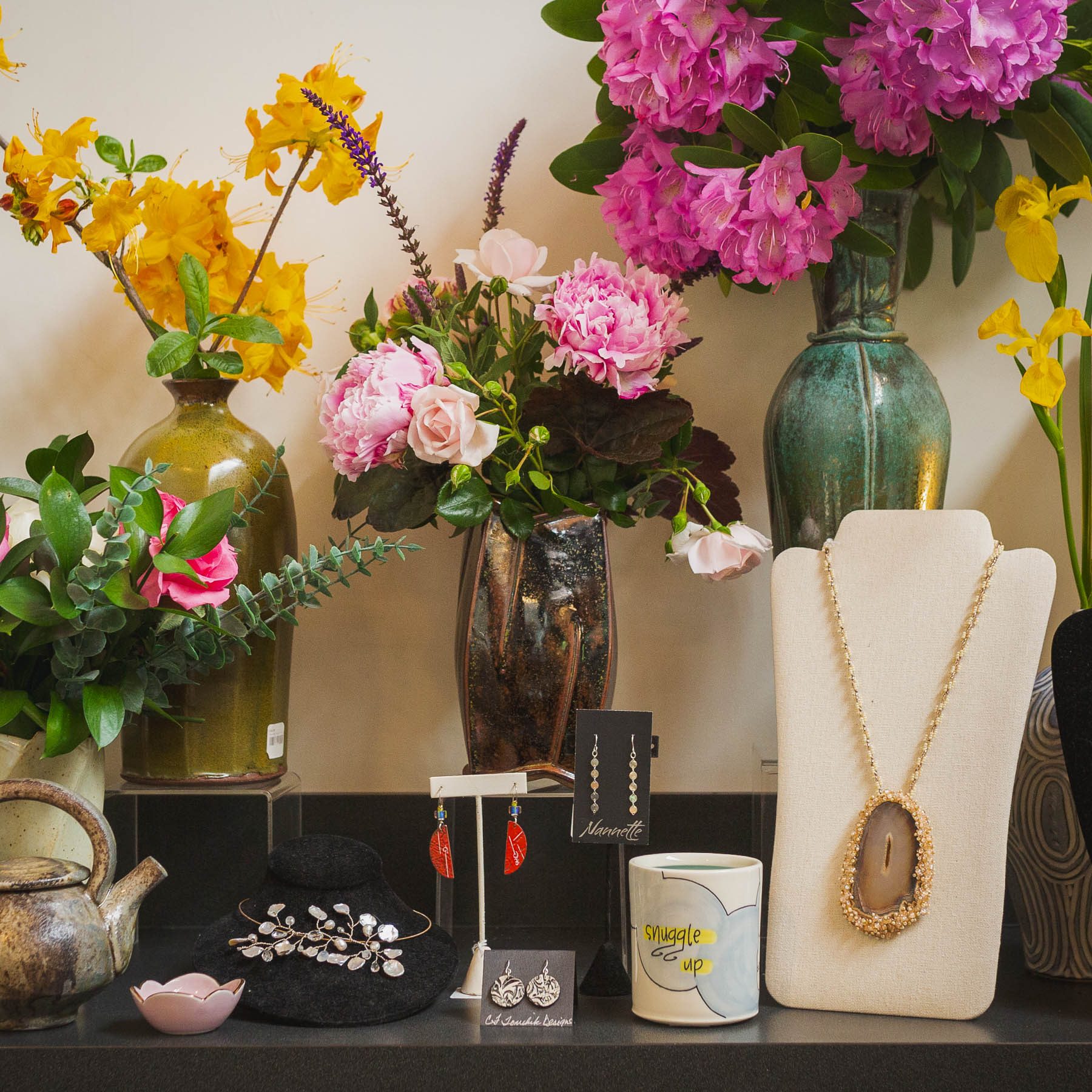 Handmade jewelry and colorful flower vases on display in a shop.
