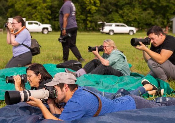 A group of photographers sitting and lying on tarps in a field taking photos.