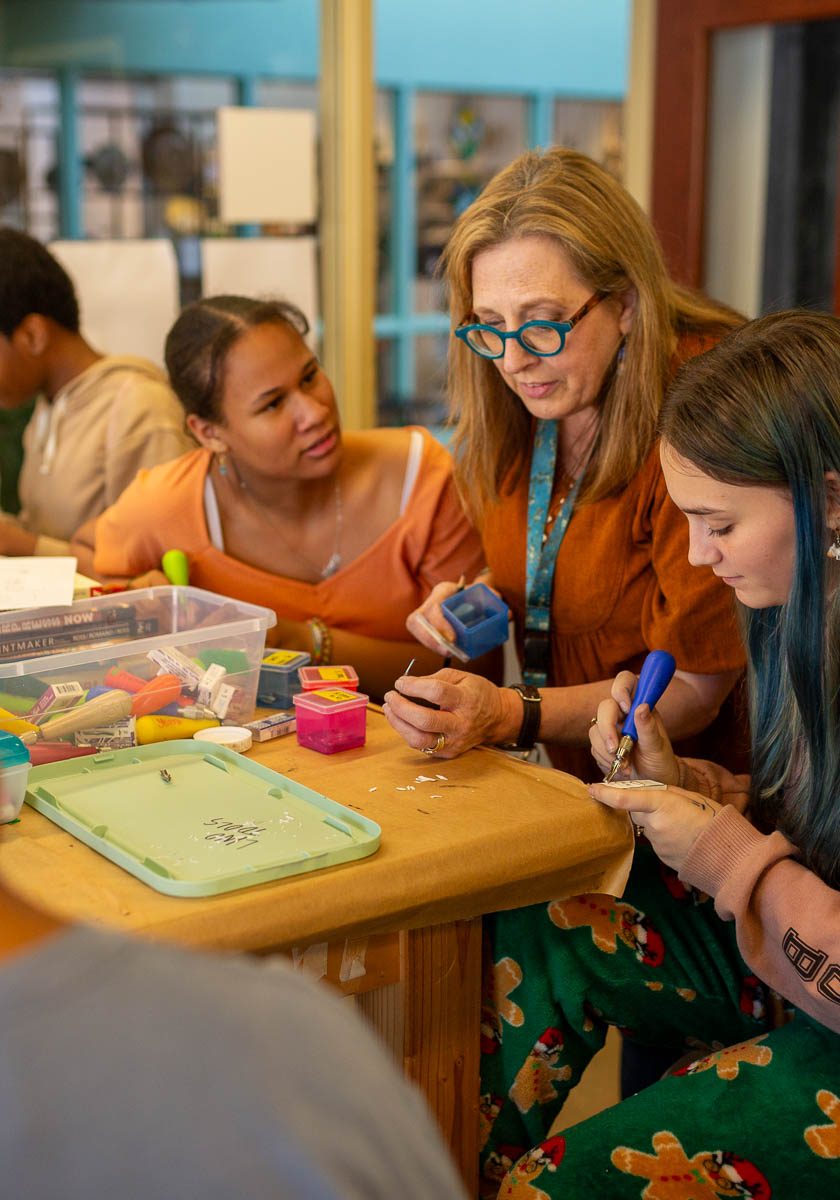 An instructor assisting students at a worktable during a group craft class.