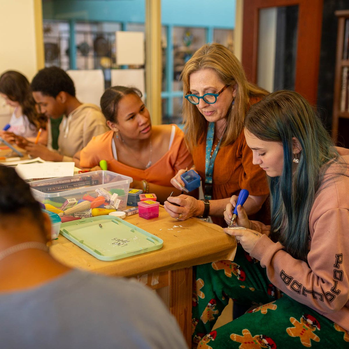 An instructor assisting students at a worktable during a group craft class.