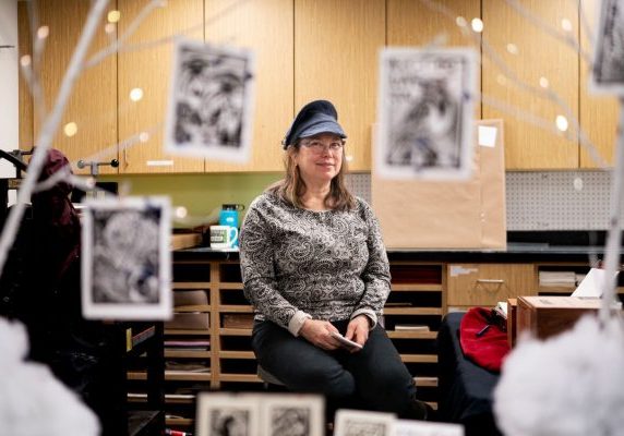 A woman in a knitted hat standing behind a table displaying black-and-white prints