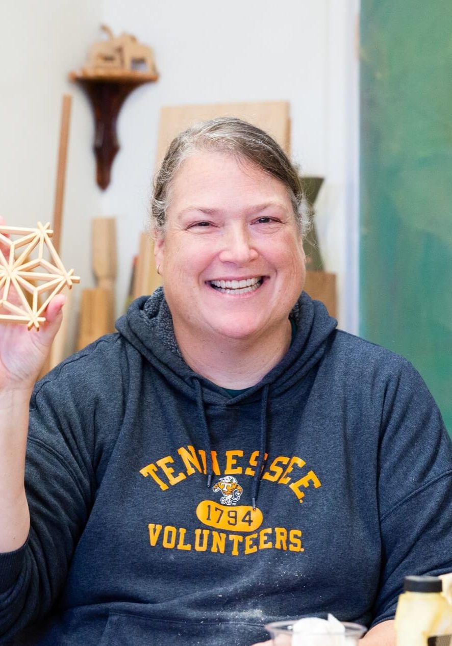 A smiling woman holding up a geometric wooden star craft.