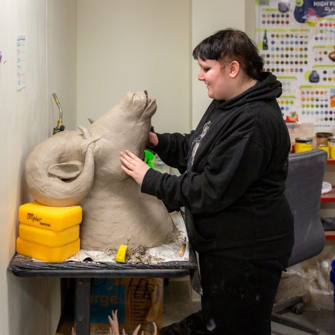 An artist sculpting a large clay bust in a ceramics studio.