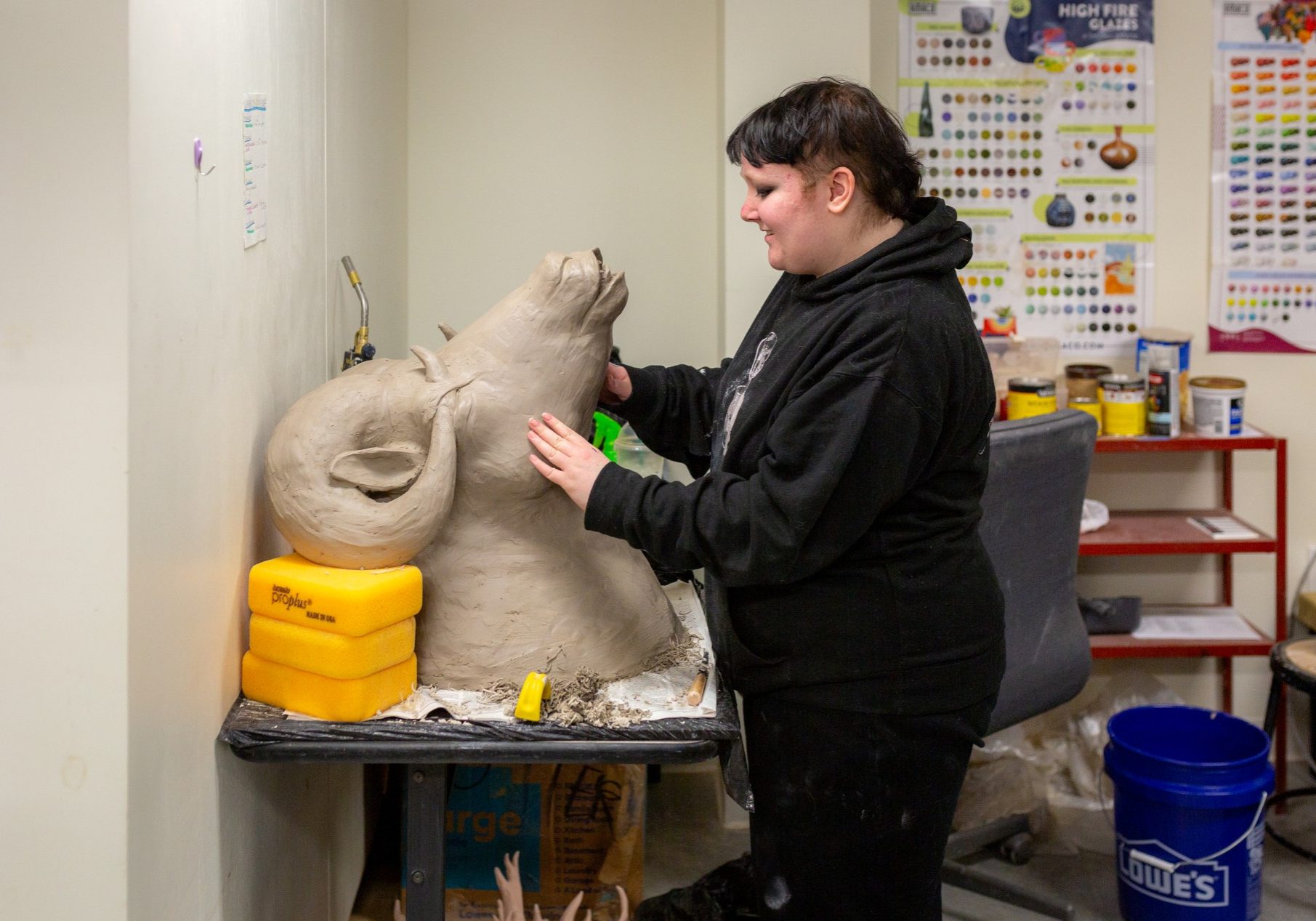 An artist sculpting a large clay bust in a ceramics studio.