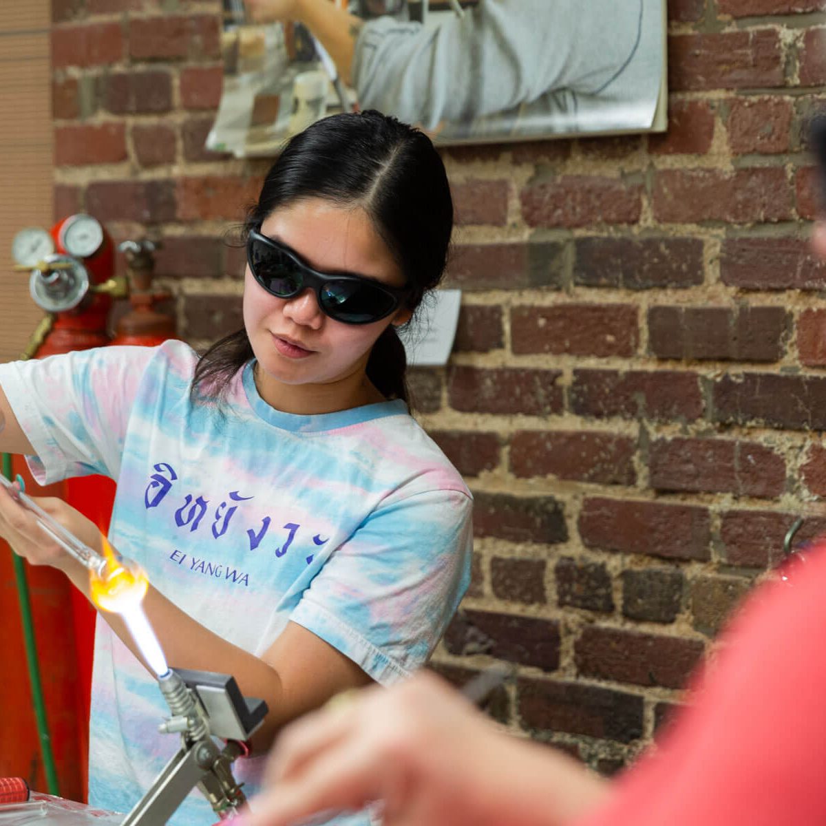 A young woman wearing safety glasses using a torch in a glassworking studio.