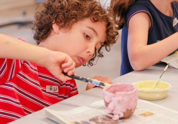 A curly-haired child painting intently with a paintbrush.