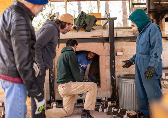 People standing around an outdoor brick kiln or furnace.