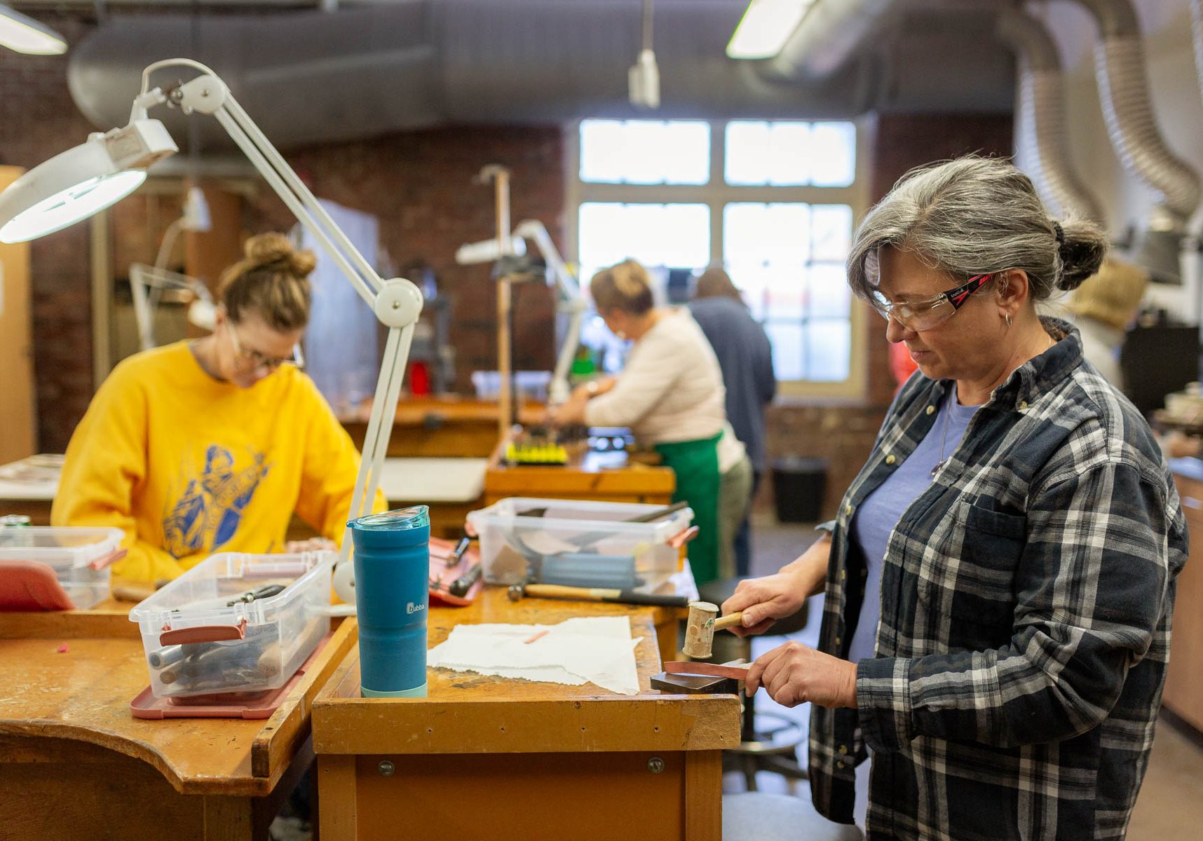 Two women working on craft projects at workbench stations in an art studio.
