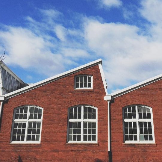 Exterior of a red brick building with large arched windows under a blue sky.