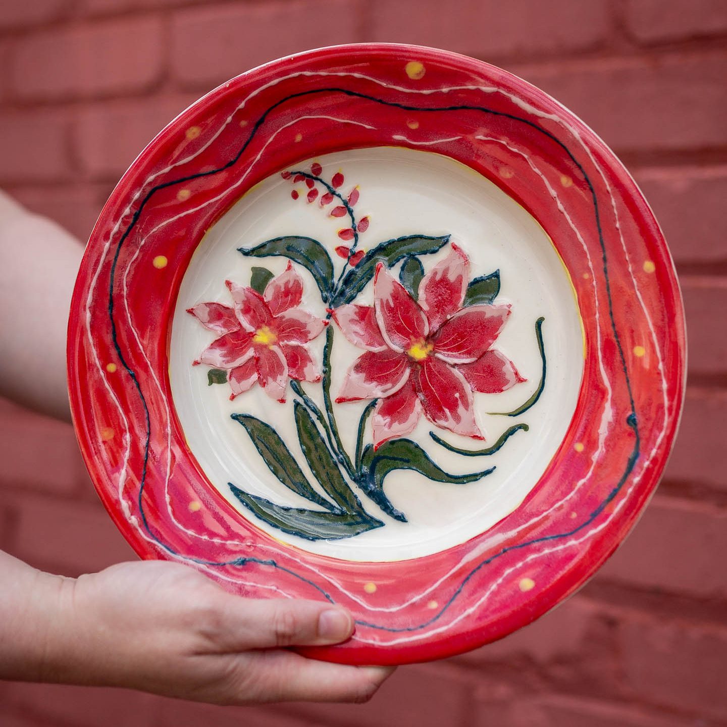 Hands holding a colorful hand-painted floral ceramic plate.